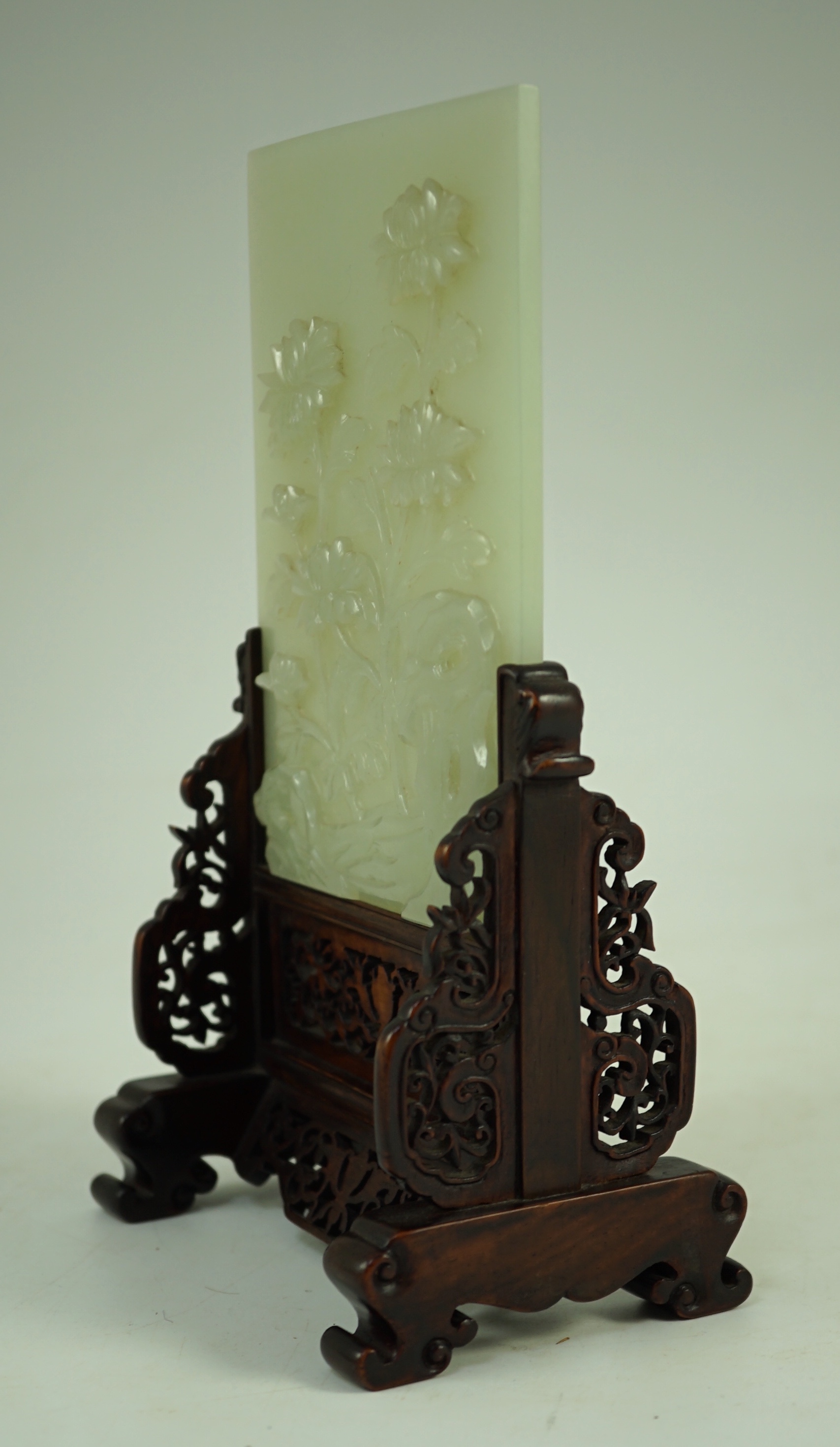 A good Chinese celadon jade ‘peonies and rockwork’ small table screen and stand, 18th/19th century, Jade 14.7 cm x 10.3cm, total size including carved wood stand 22cm x 12.3cm
